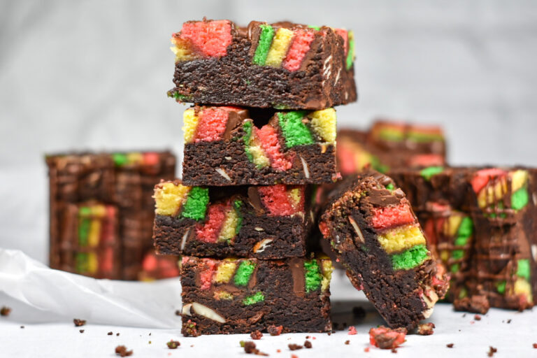 A stack of Italian rainbow brownies on a white background, surrounded by crumbs