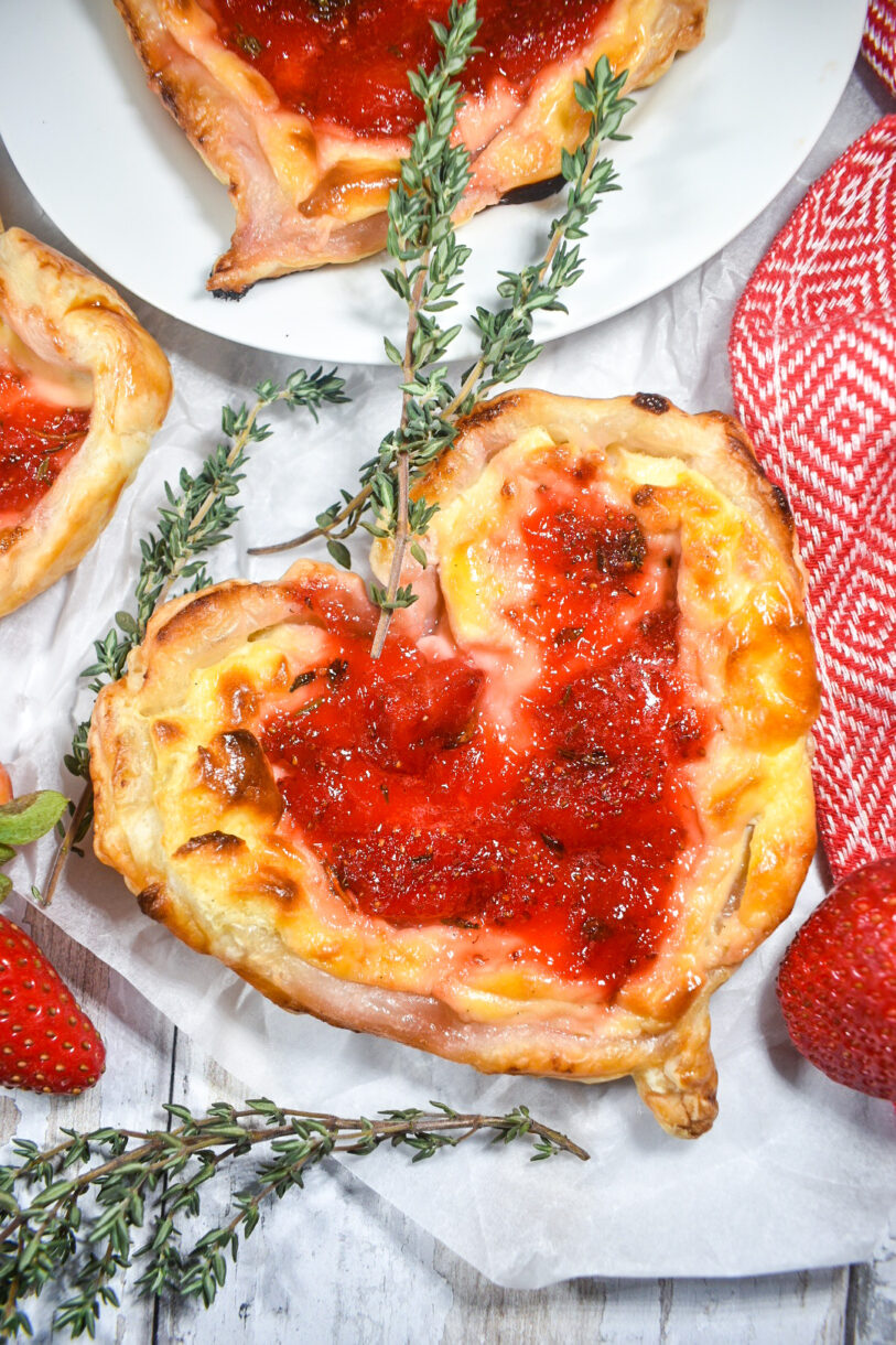 Puff pastry hearts on a white background, surrounded by strawberries and sprigs of fresh thyme