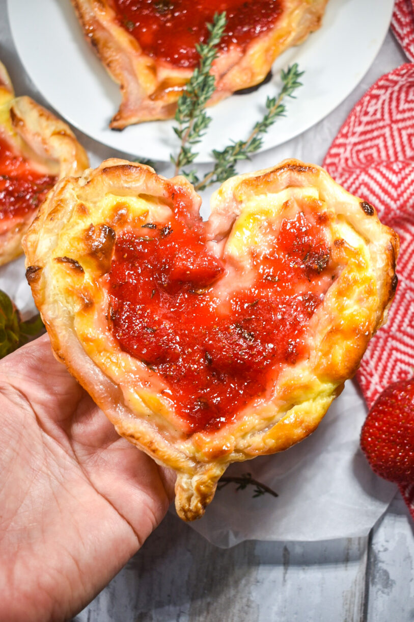 A hand holding a heart with puff pastry and strawberries