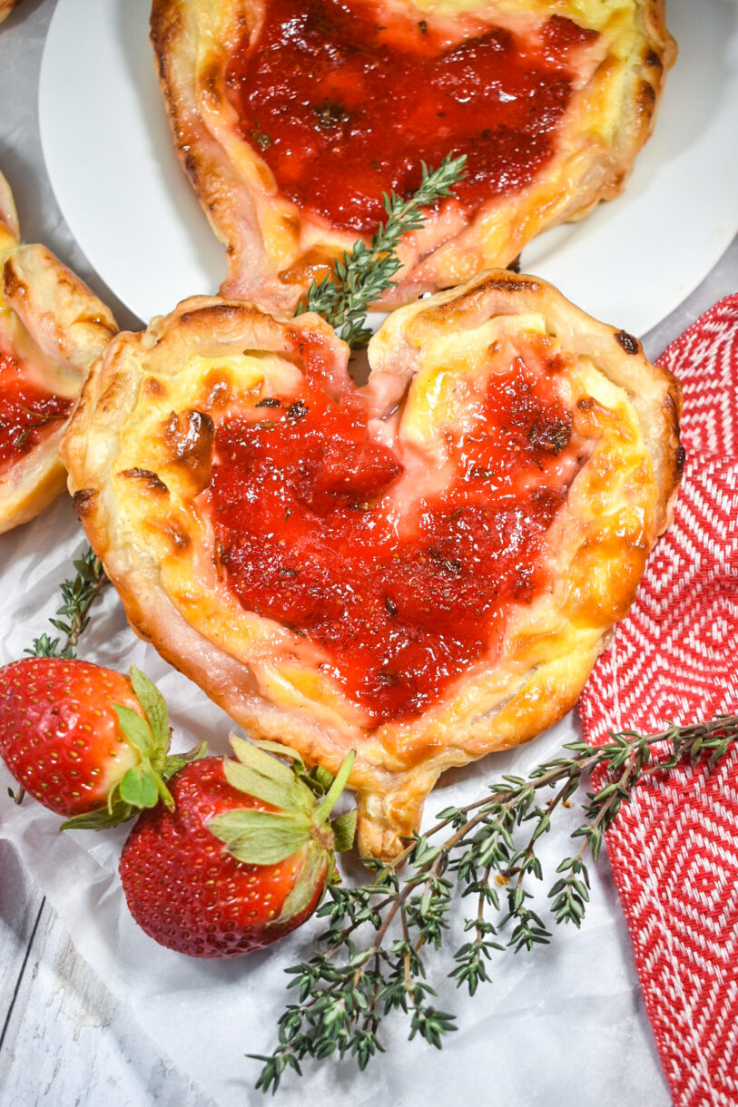 Strawberry puff pastry hearts with strawberry jam, on a white background with a sprig of thyme and red berries