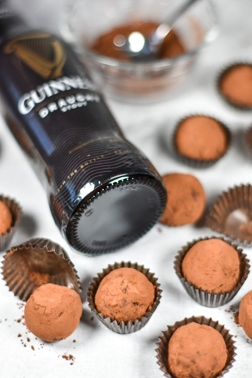 The cap of a bottle of beer, surrounded by a bowl of cocoa, a spoon, and Guinness and dark chocolate truffles