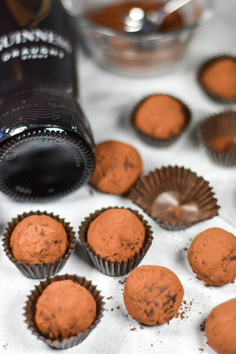 Guinness and dark chocolate truffles, a bowl of cocoa powder, and a bottle of beer