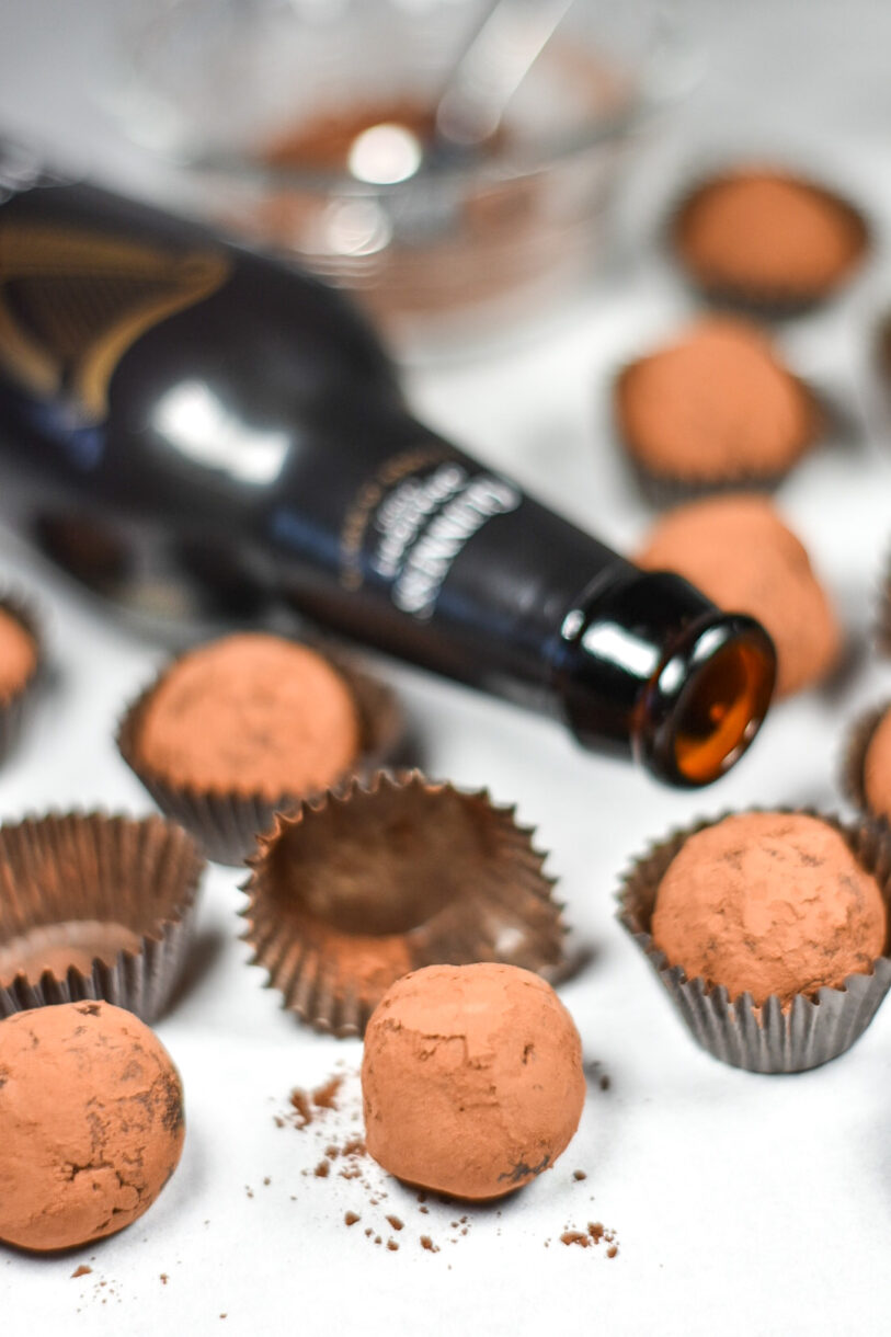A bottle of Guinness beer surrounded by brown truffle cups and dark chocolate truffles coated in cocoa powder