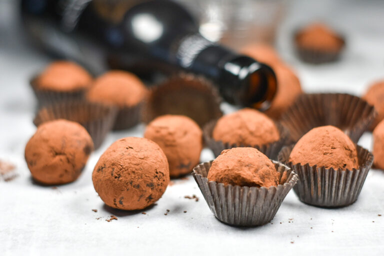 Dark chocolate truffles in brown paper truffle cups, arranged on a white surface with bottle of beer