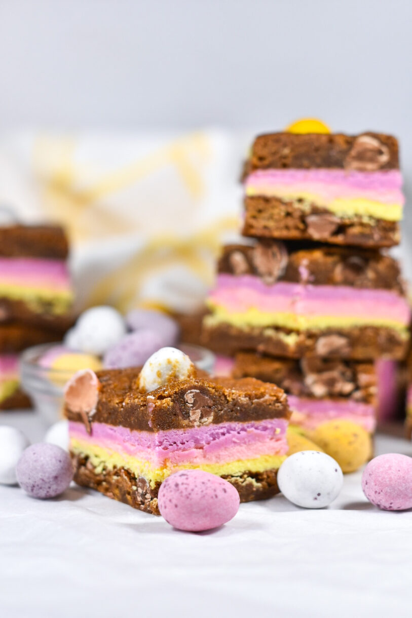 Blonde brownies with layers of pastel-colored ganache, surrounded by mini eggs