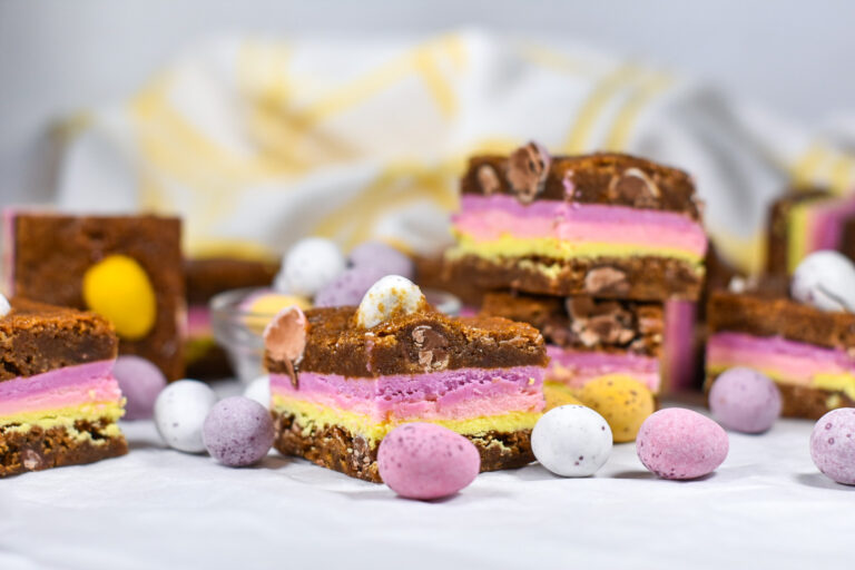 Cadbury egg blondies with layers of pastel-colored ganache, surrounded by mini eggs