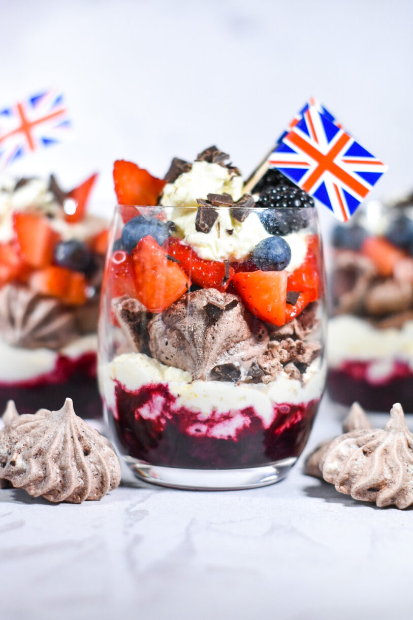 Triple Berry Eton Mess with Chocolate Meringue, layered in a glass with miniature British flags, surrounded by chocolate meringue cookies