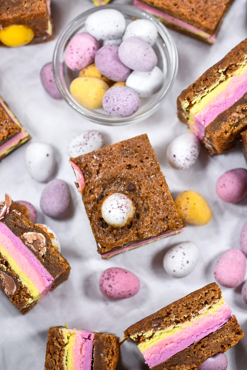 A glass bowl of mini eggs and blondies on a white background