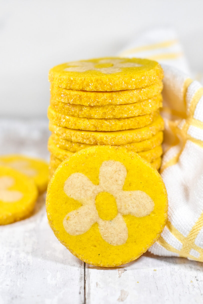 Lemon daisy cookie stack, with a single cookie propped in front, on a white wood surface