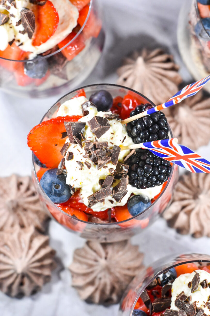 Looking down into a glass of Eton Mess, with a white background and chocolate meringue kisses surrounding
