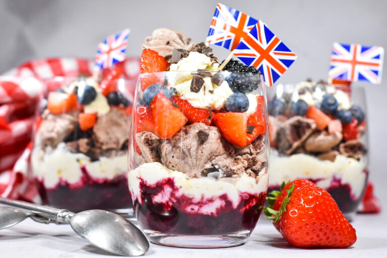 Triple Berry Eton Mess with Chocolate Meringue in clear glasses, with a spoon and strawberries nearby
