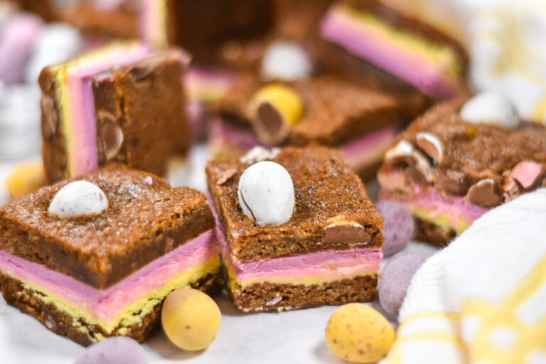 Cadbury mini egg blondies with layers of pastel-colored ganache, surrounded by mini eggs and a yellow and white towel