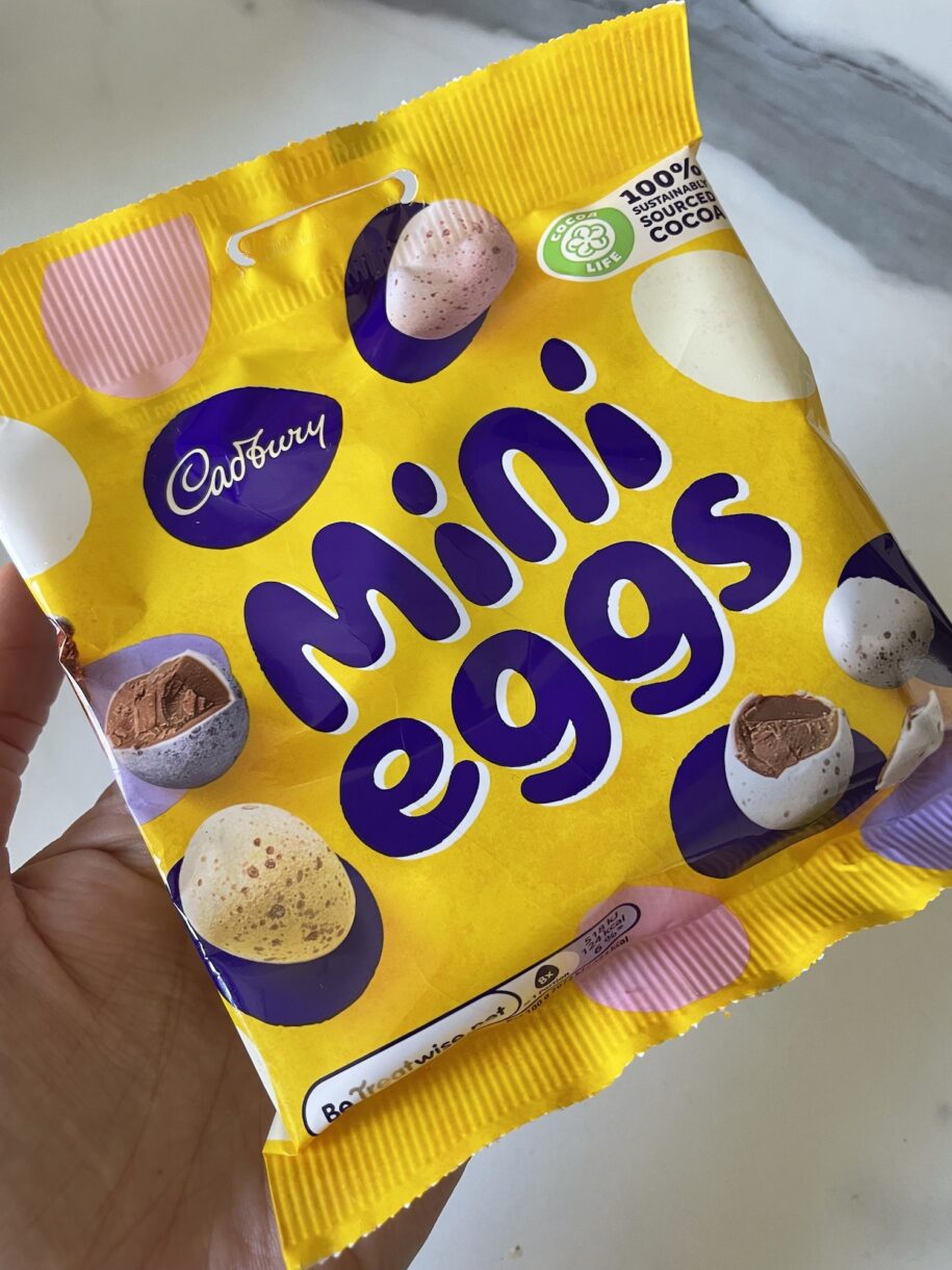Hand holding a yellow bag of Cadbury mini eggs