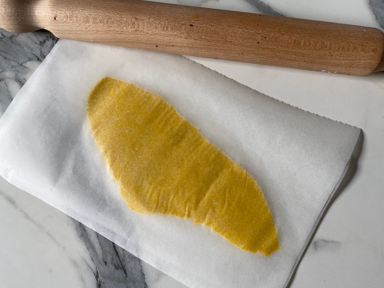 Yellow dough rolled between sheets of parchment