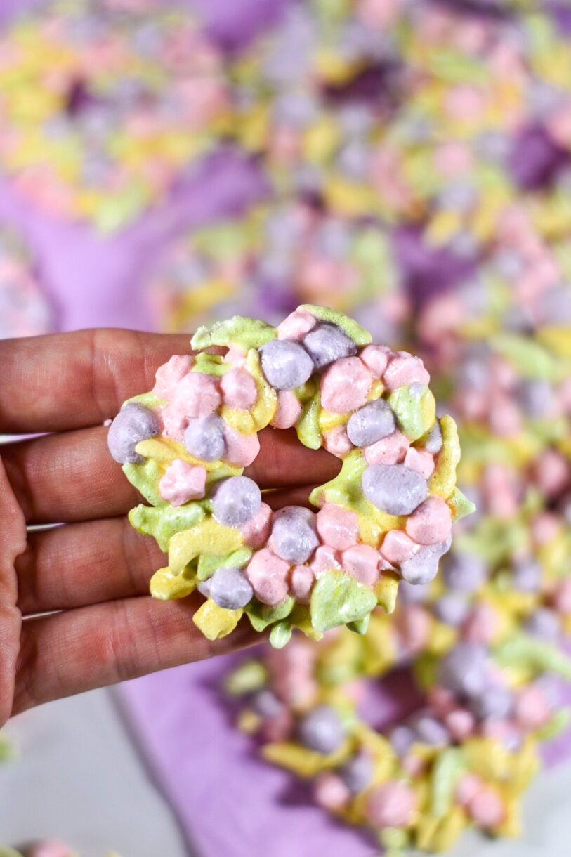 Hand holding a meringue wreath cookie made from this floral wreath meringue cookies recipe