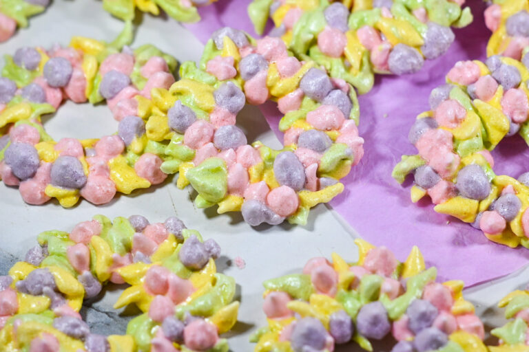 Piped meringue wreath cookies recipe in pink, purple, green and yellow, on a white background with purple tissue