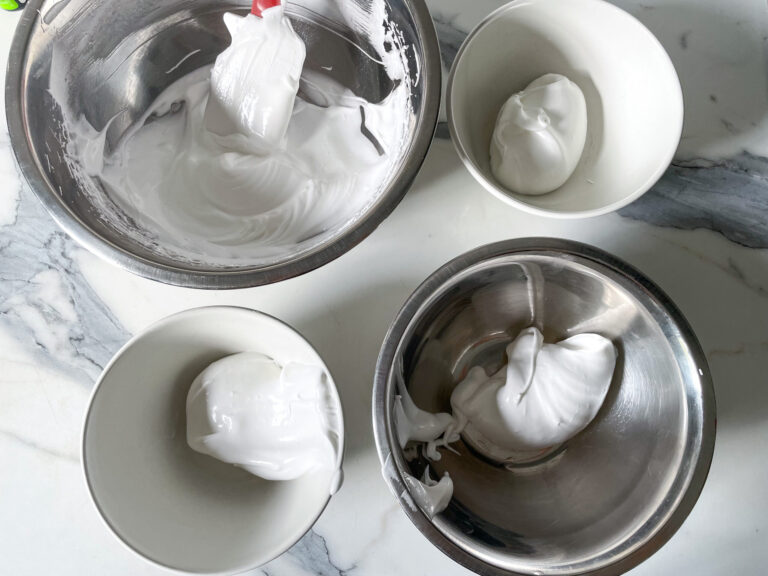 Four bowls of meringue arranged on a marble counter, preparing to make piped meringue cookies recipe