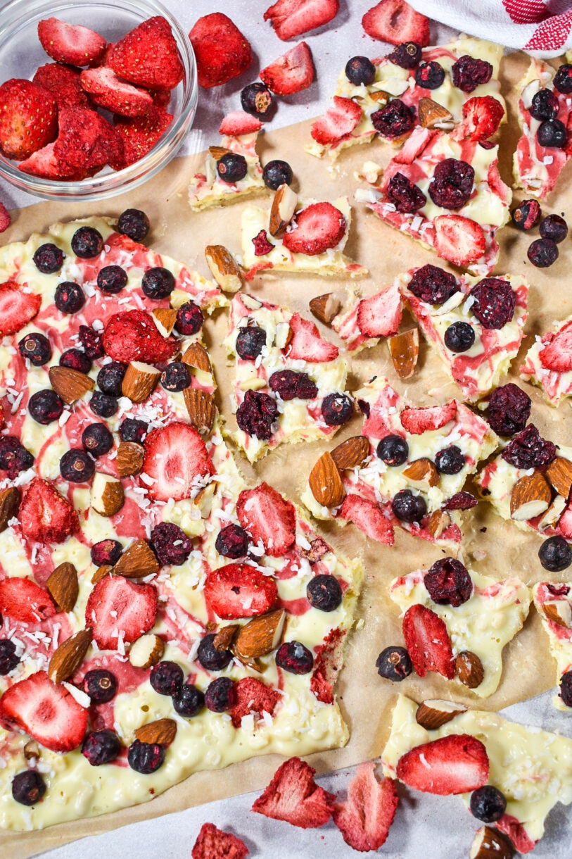 White chocolate berry bark scattered across a sheet of brown baking parchment, made from an original white chocolate bark recipe