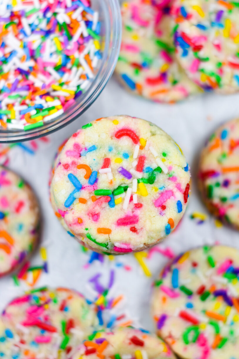 Closeup of rainbow funfetti shortbread cookies, and a bowl of sprinkles