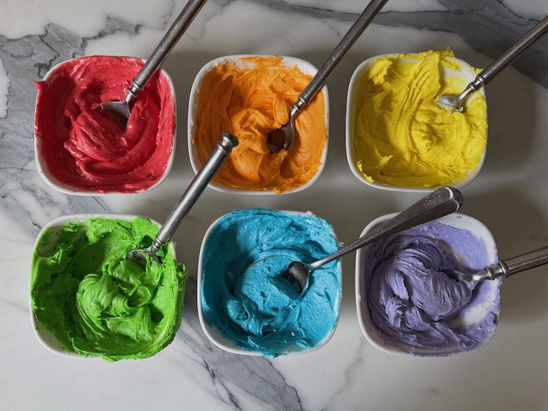 bowls of rainbow colored buttercream with spoons