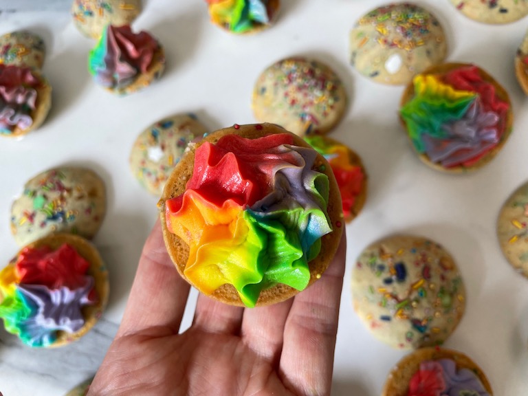 hand holding a whoopie pie with rainbow buttercream