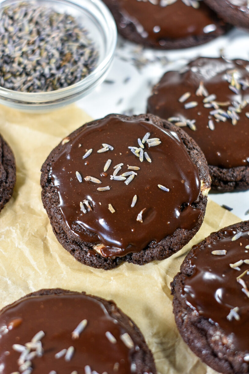 Closeup of a dark chocolate cookie with dark chocolate ganache and dried lavender buds, on a sheet of brown parchment