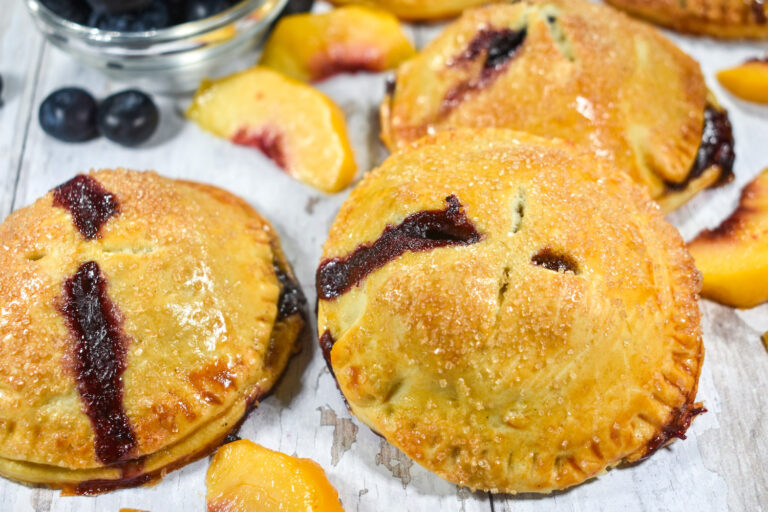 Peach hand pies arranged on a white surface with fresh fruit
