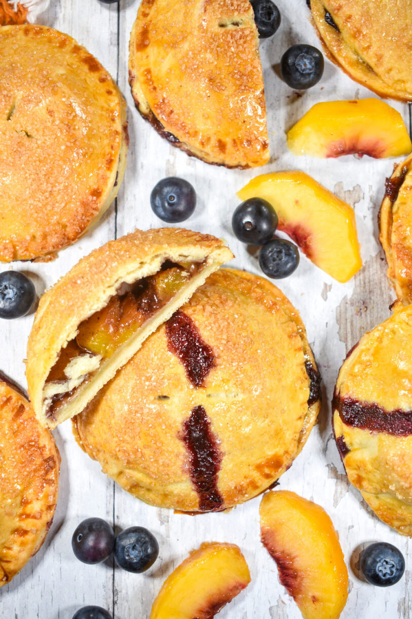 Peach hand pies, blueberries, and peaches on a white surface