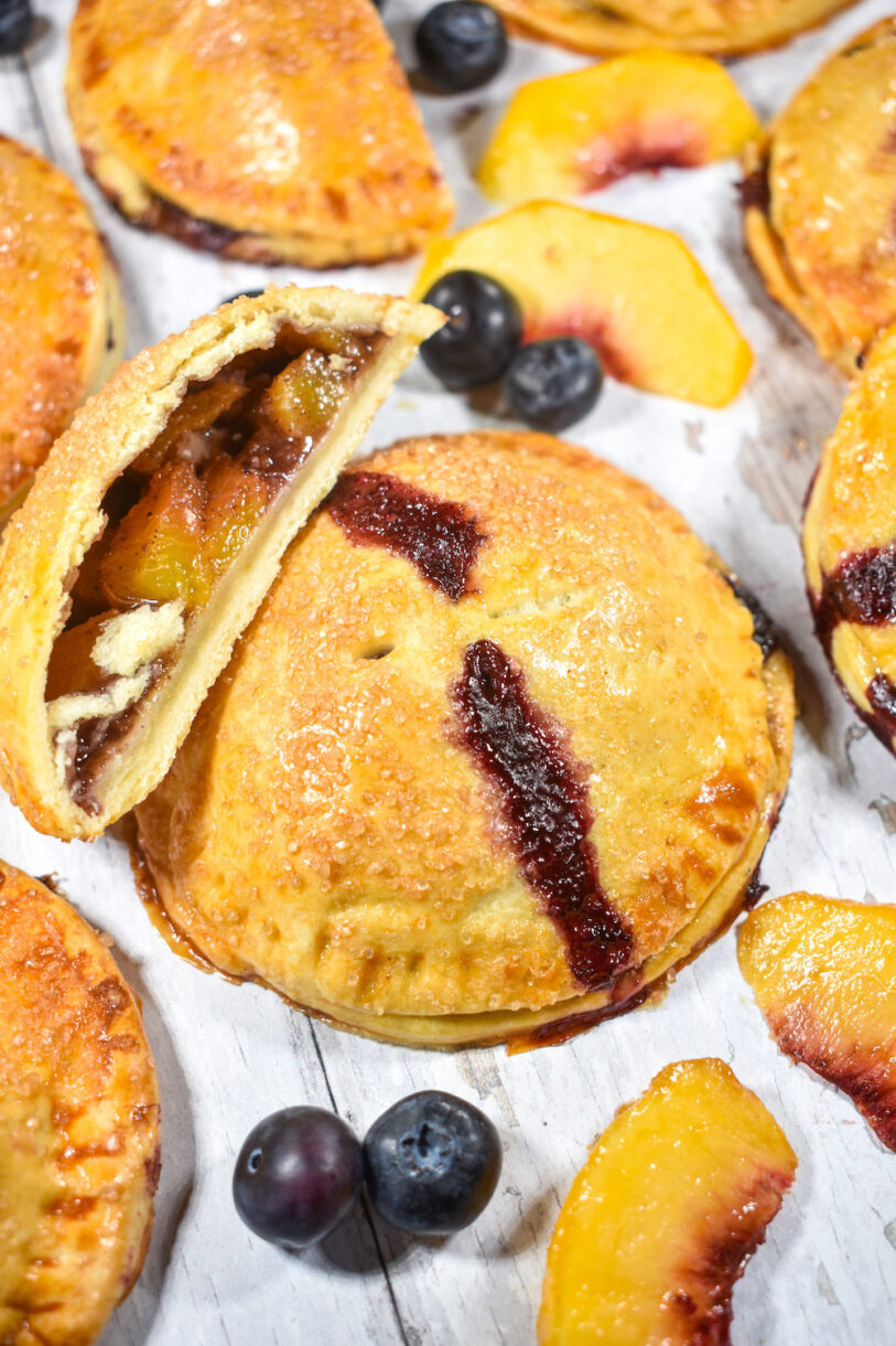 Hand peach pies arranged on a white surface with fresh fruit