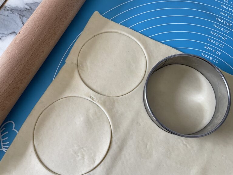 Sheet of pastry cut into discs, with cutter and rolling pin