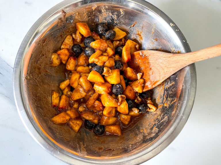 Peach and blueberry mixture in a bowl, with wooden spoon