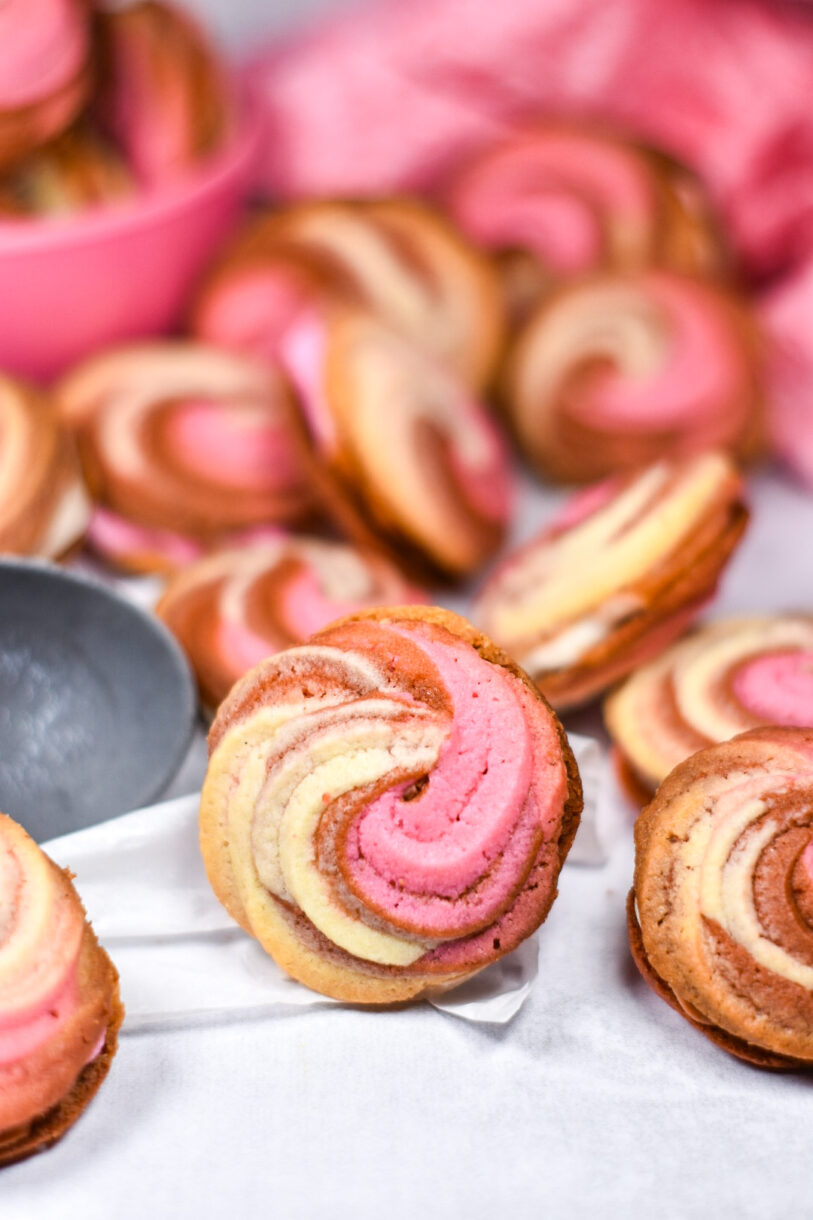 Neapolitan cookies arranged on a white surface, with pink bowl in the background