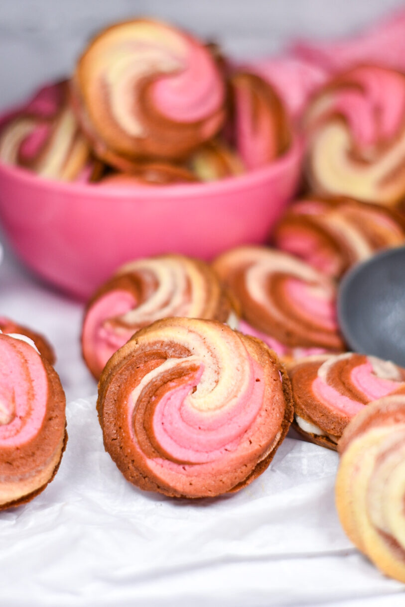 Neapolitan butter cookies, made from an original butter cookie recipe, arranged on a white surface with pink bowl of cookies in the background