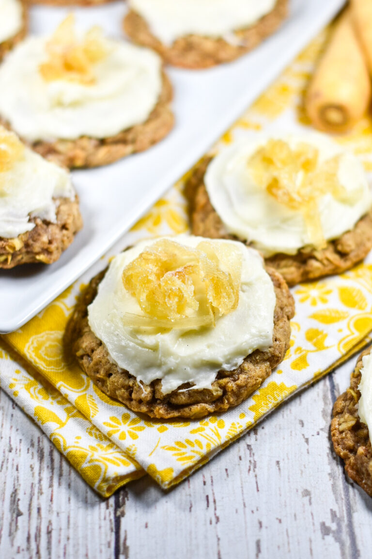 Parsnip cookies on a white wood surface with white plate, yellow dish towel, and two parsnips