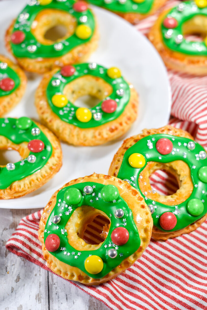 Wreath shaped Nutella hand pies with green glaze and candy decorations, and red tea towel, on a white background