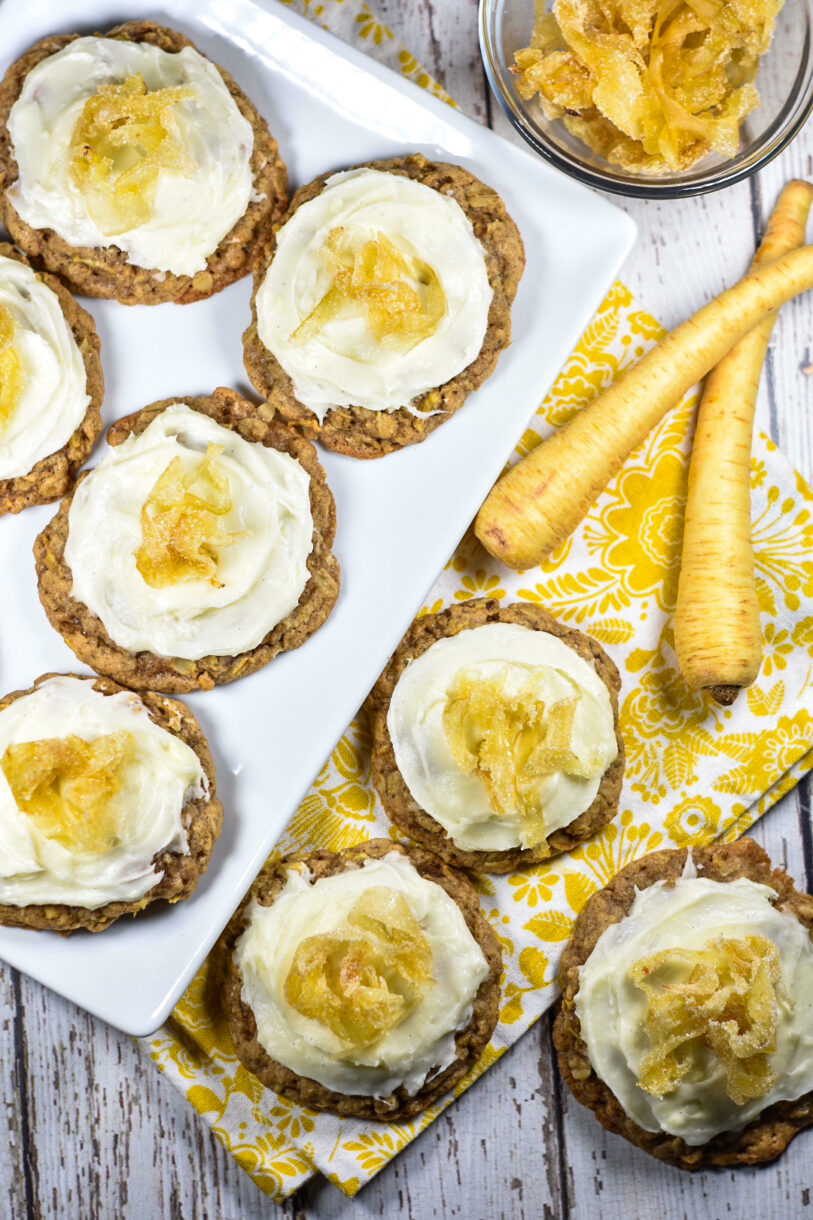 Parsnip cookies on a white wood surface with white plate, yellow dish towel, and two parsnips
