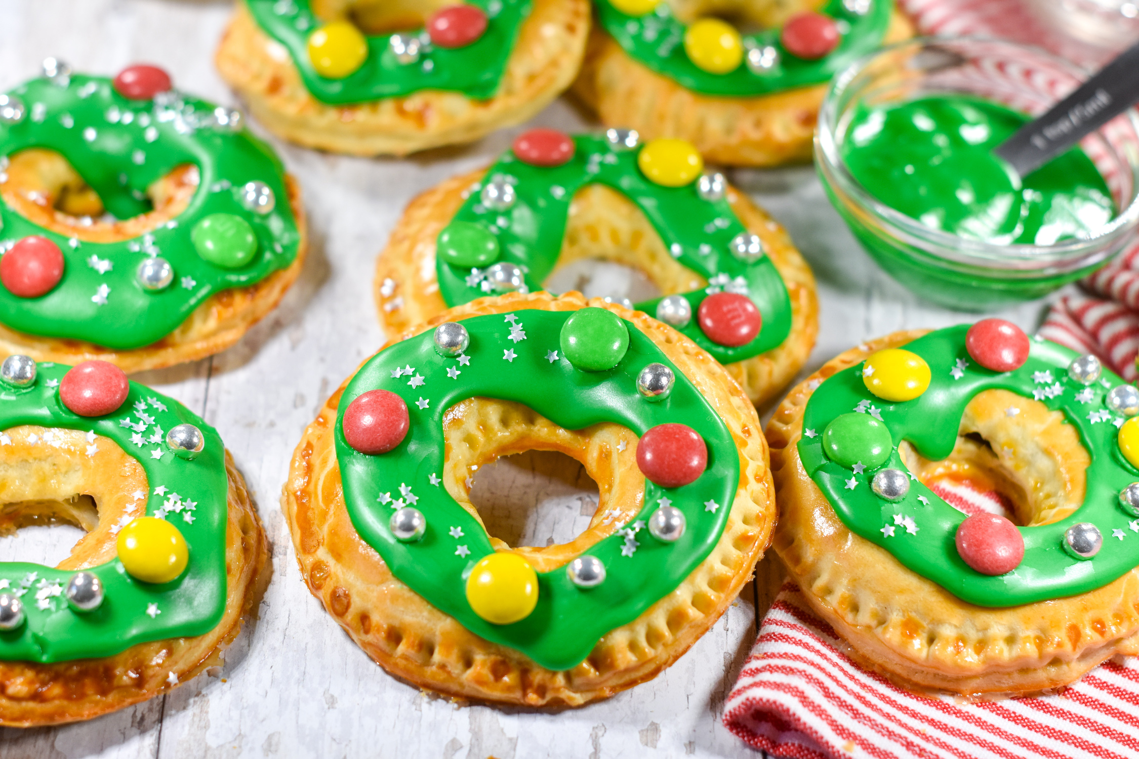 Pastry wreaths with green icing and colorful decorations, with a red and white tea towel