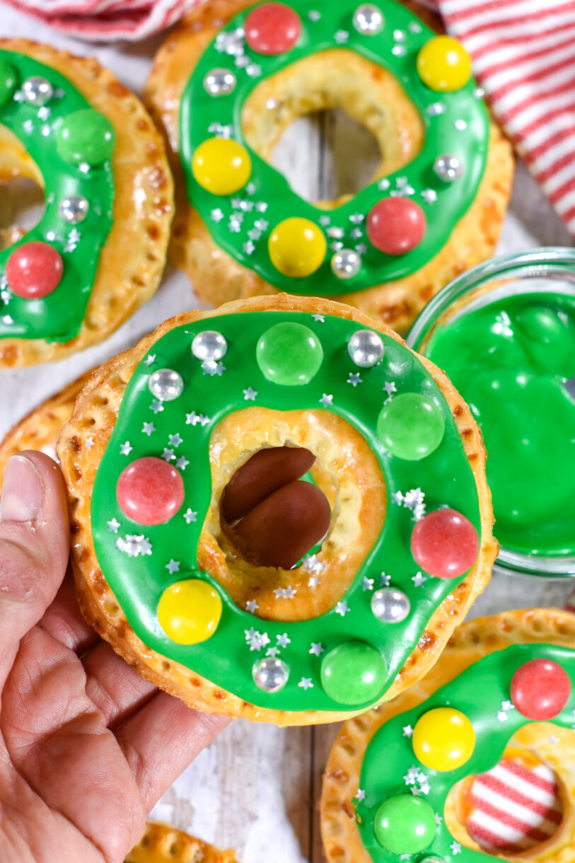 Hand holding a wreath shaped pastry with green frosting and candy decorations