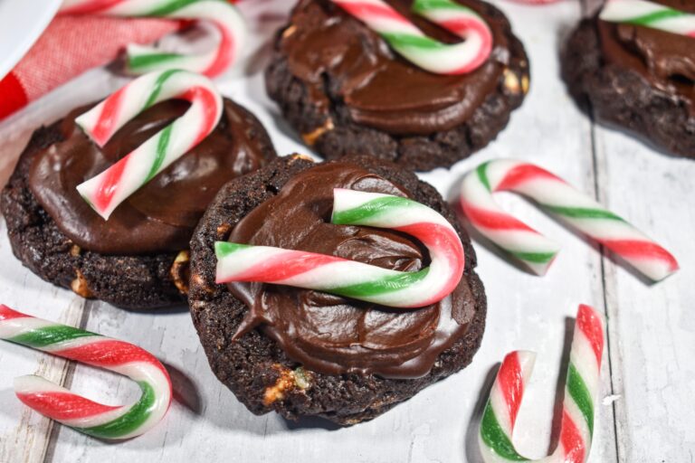 Dark chocolate mint candy cane cookies, mini candy canes, and a red gingham tea towel, on a white wooden surface