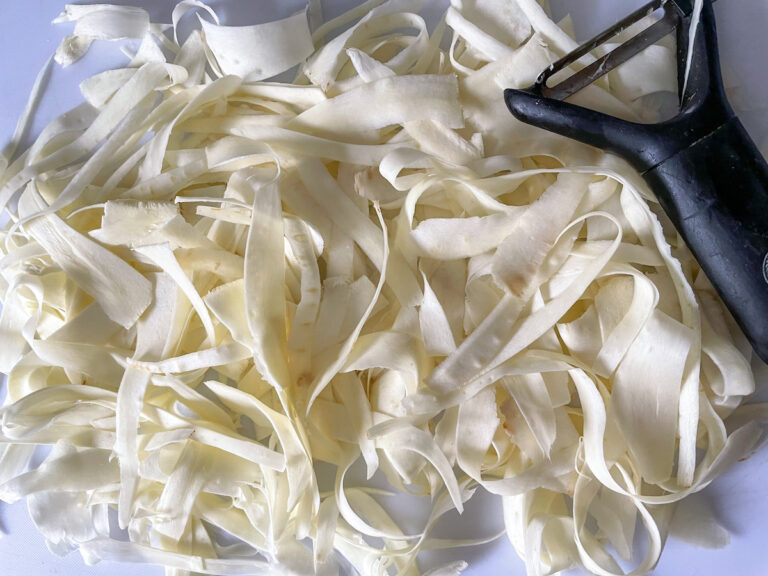 Strips of raw parsnip and a vegetable peeler