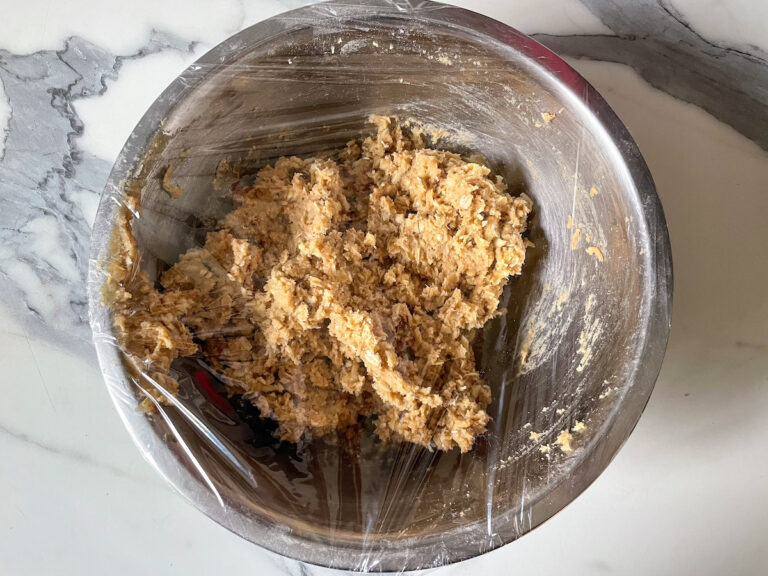Bowl filled with cookie dough, with plastic wrap stretched over the top
