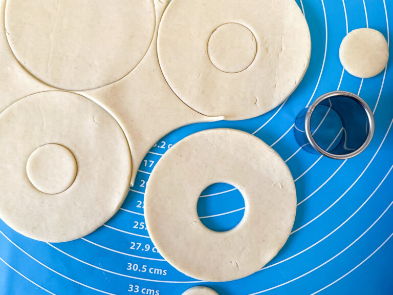 Closeup of a small round cutter and discs of shortcrust pastry on a blue mat