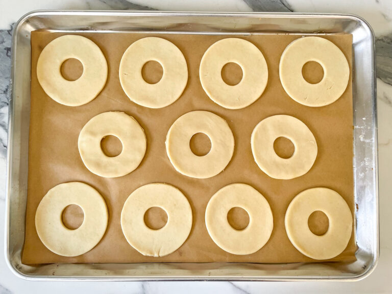 A metal tray lined with parchment, with rows of ring shaped shortcrust pastry