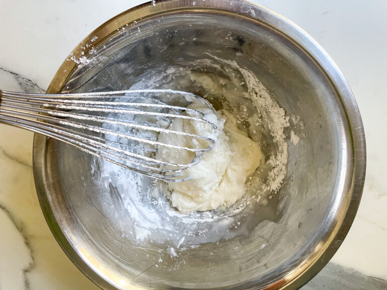 A whisk in a metal bowl with confectioner's sugar