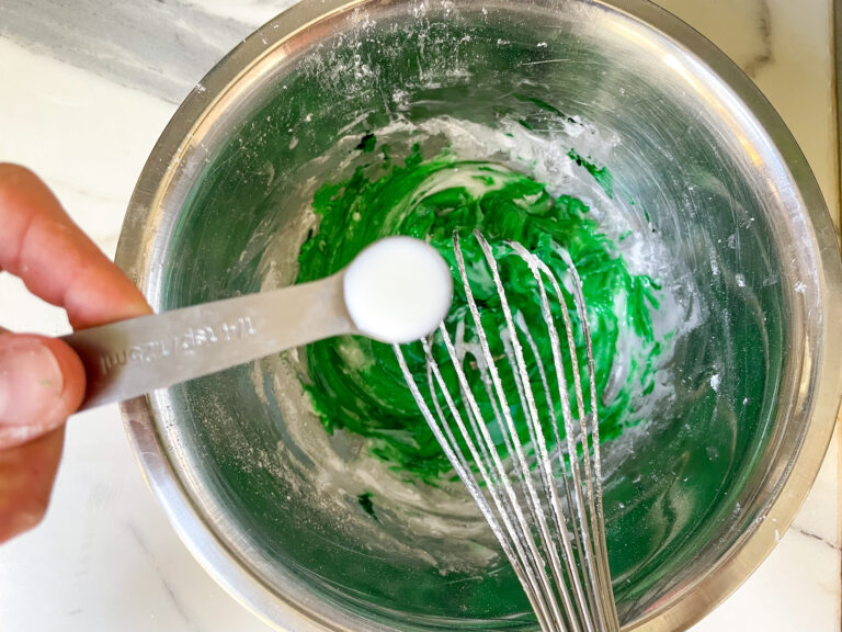 A small spoon of milk, over top of a metal mixing bowl filled with green glaze