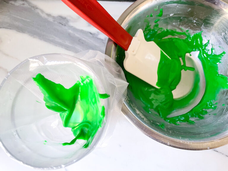 A metal bowl of green glaze with a spatula, next to a piping bag