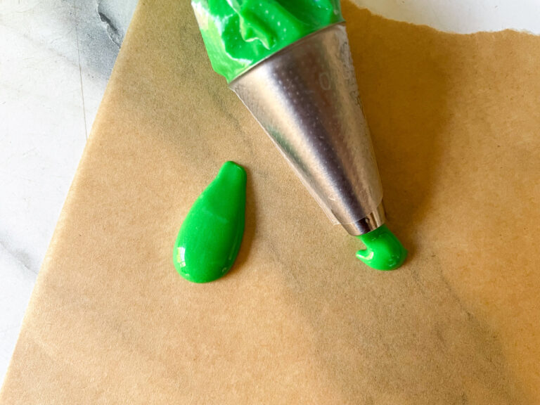 A piping tip testing green glaze on a sheet of baking parchment