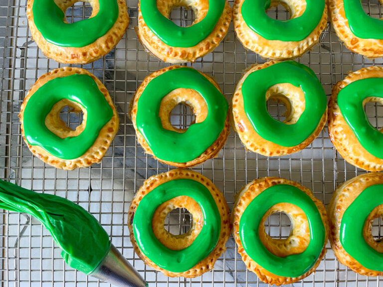 Green wreath pastries on a wire cooling rack with a piping bag of icing