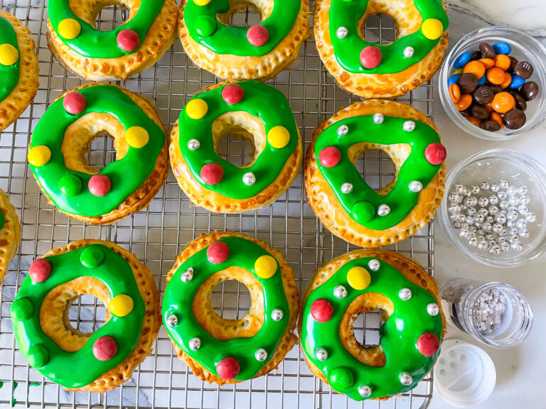 Wreath pastries with green frosting, and bowls of decorations on the side