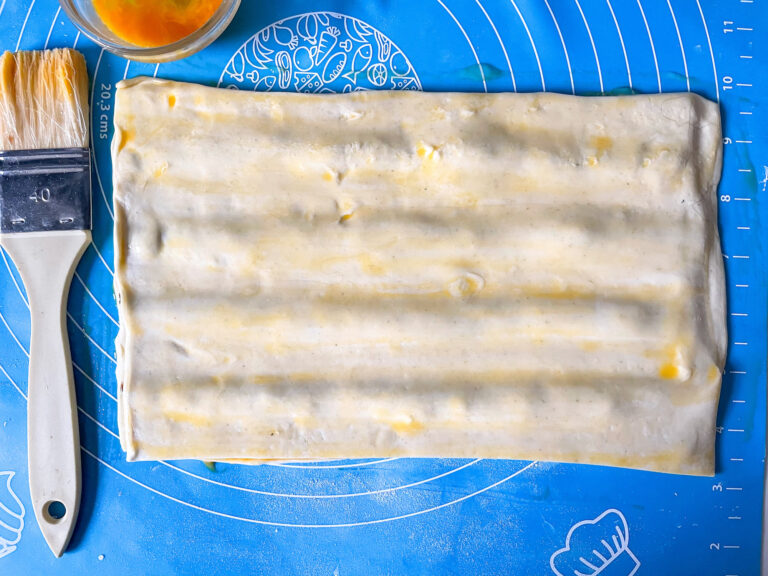 Puff pastry on a silicone mat with a pastry brush and dish of egg wash